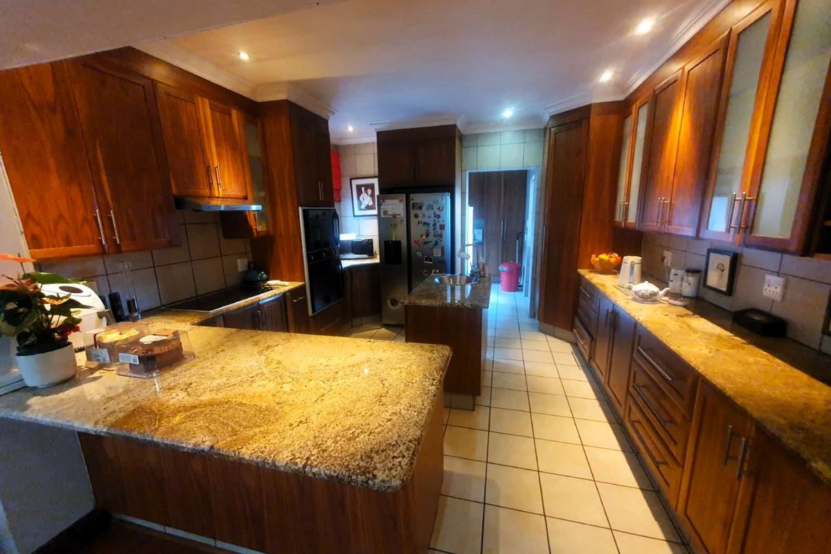 Spacious kitchen featuring warm wooden cabinetry, granite countertops, a central island, and tiled flooring with integrated appliances.