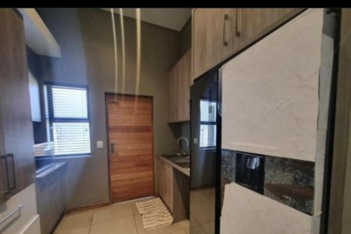 A functional kitchen featuring modern wood-veneer cabinetry, tiled flooring, and a stainless steel sink, providing a clean and practical workspace.