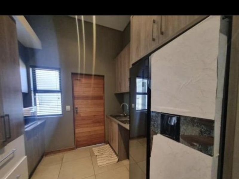 A functional kitchen featuring modern wood-veneer cabinetry, tiled flooring, and a stainless steel sink, providing a clean and practical workspace.