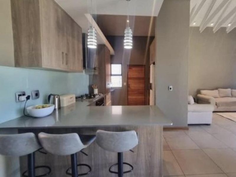 Modern open-plan kitchen featuring stone countertops, sleek cabinetry, and a breakfast bar, seamlessly flowing into the adjacent living area with tiled flooring.