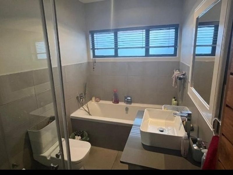 Modern bathroom featuring a built-in bathtub, glass-enclosed shower, vessel sink vanity, and neutral wall tiling with horizontal window blinds.
