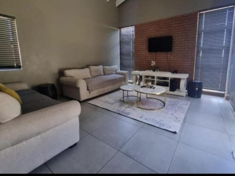 Spacious living room featuring a striking exposed brick feature wall, large format floor tiles, and vaulted ceilings with natural light through venetian blinds.