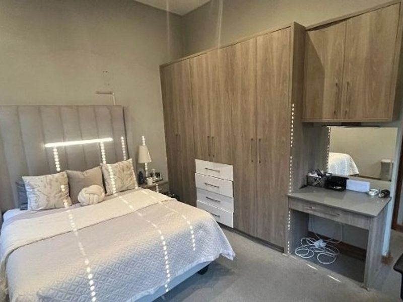 A well-appointed bedroom featuring extensive built-in wooden cabinetry, integrated storage, and a dedicated vanity area with mirror.