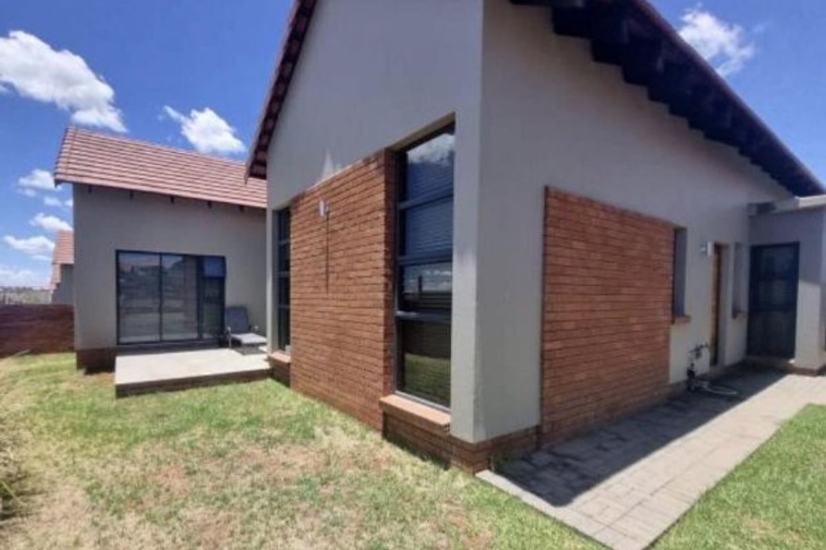 Rear view of a townhouse featuring a combination of brick and plastered exterior walls, a tiled roof, and a paved patio area.
