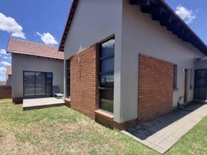 Rear view of a townhouse featuring a combination of brick and plastered exterior walls, a tiled roof, and a paved patio area.