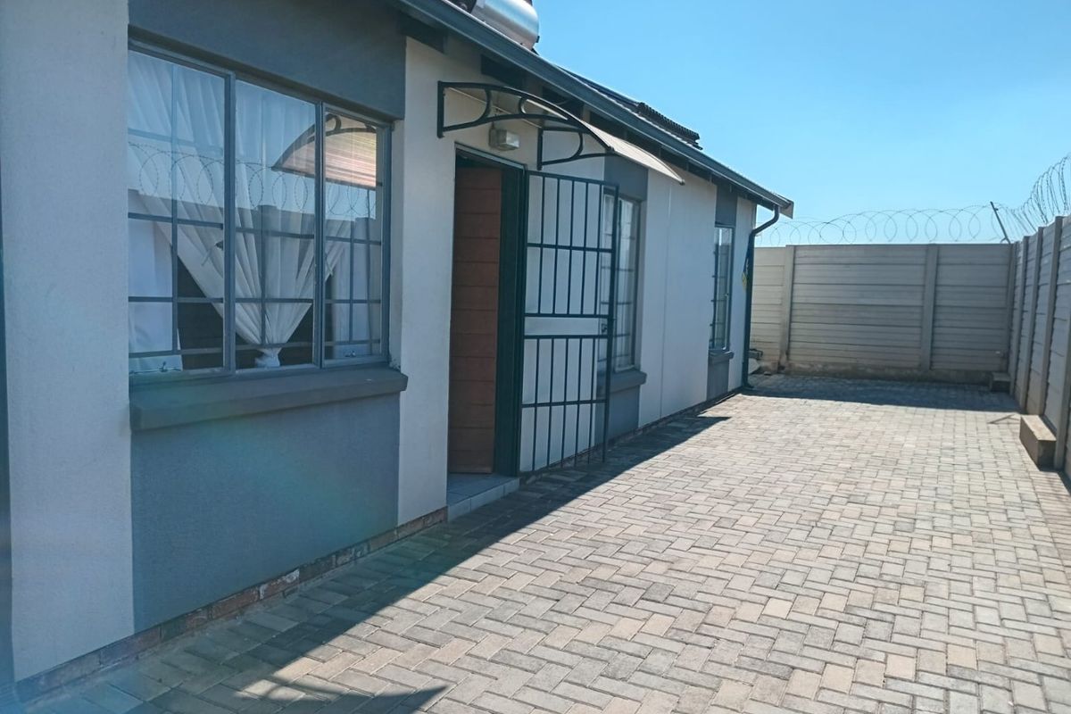 Rear exterior view of the property featuring paved courtyard, security gate, solar water heater, and perimeter wall with razor wire fencing.