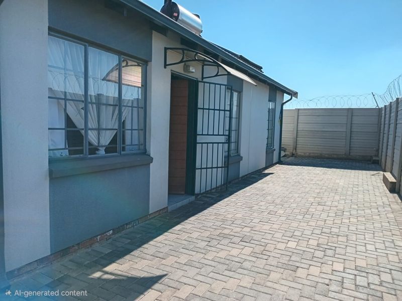 Rear exterior view of the property featuring paved courtyard, security gate, solar water heater, and perimeter wall with razor wire fencing.