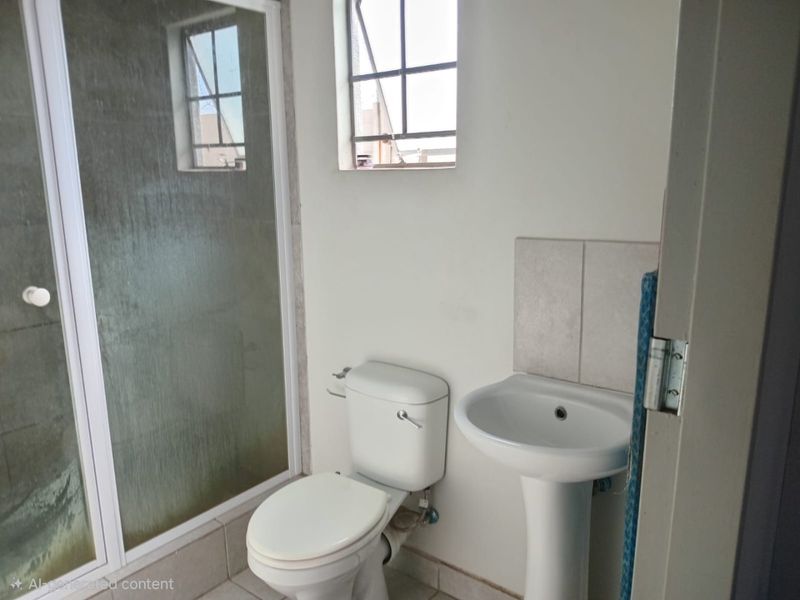 A functional bathroom featuring a pedestal basin, toilet, and a glass-enclosed shower with tiled flooring and natural light.