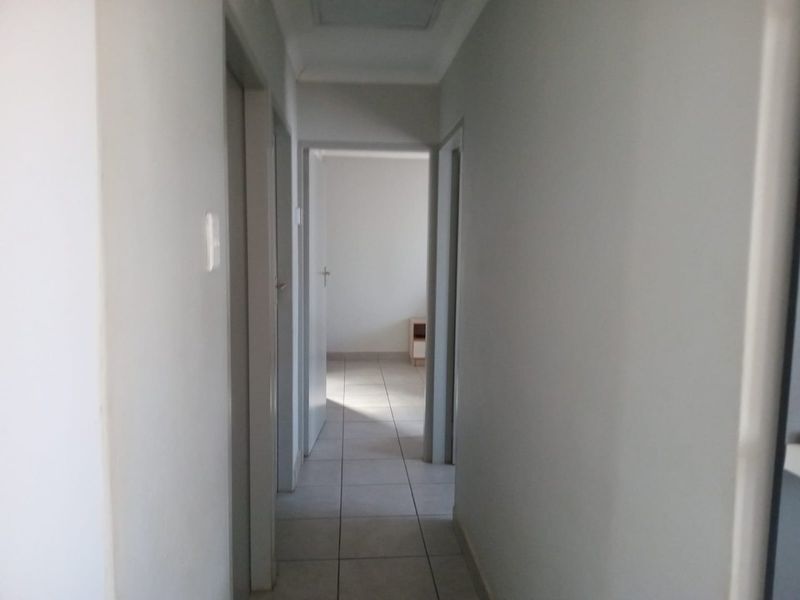 A simple, neutral-toned hallway featuring tiled flooring and access to multiple rooms, providing a clean and functional transition space within the home.