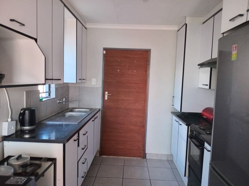 A functional galley-style kitchen featuring white cabinetry, dark countertops, tiled flooring, and a built-in oven with an extractor fan.