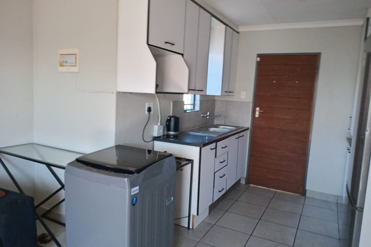 A functional kitchen featuring white built-in cabinetry, laminate countertops, a stainless steel sink, and tiled flooring with direct access to an internal door.