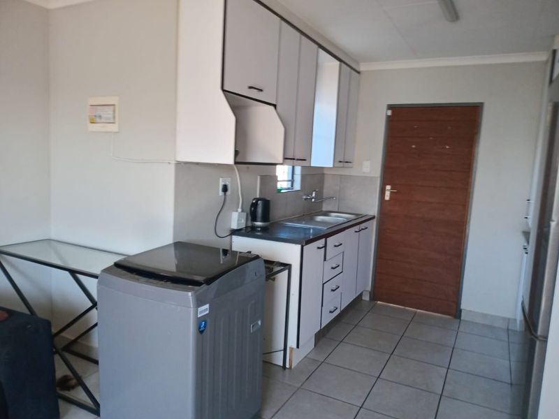 A functional kitchen featuring white built-in cabinetry, laminate countertops, a stainless steel sink, and tiled flooring with direct access to an internal door.