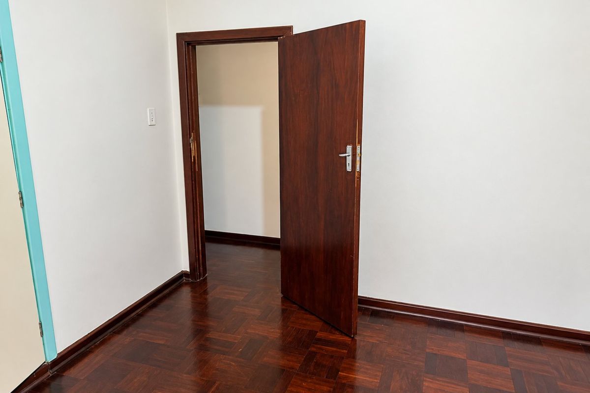 An empty bedroom featuring classic parquet flooring and a solid wooden door, providing a clean and neutral space ready for personalization.