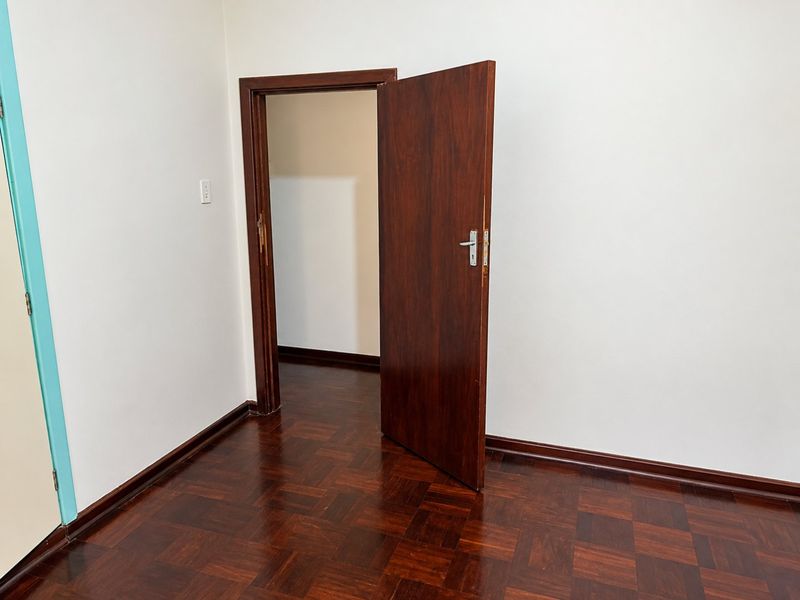 An empty bedroom featuring classic parquet flooring and a solid wooden door, providing a clean and neutral space ready for personalization.