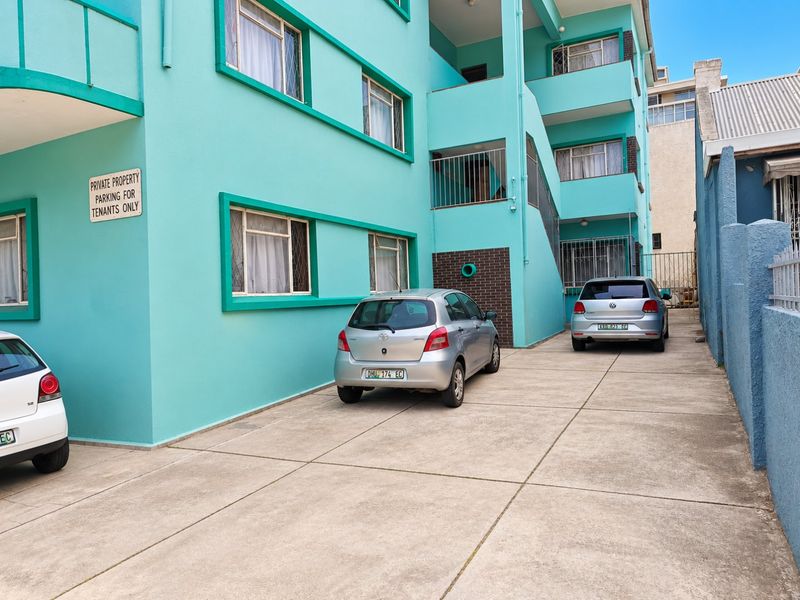 Exterior view of an apartment building facade featuring a concrete driveway, parking area, and external access stairwell.