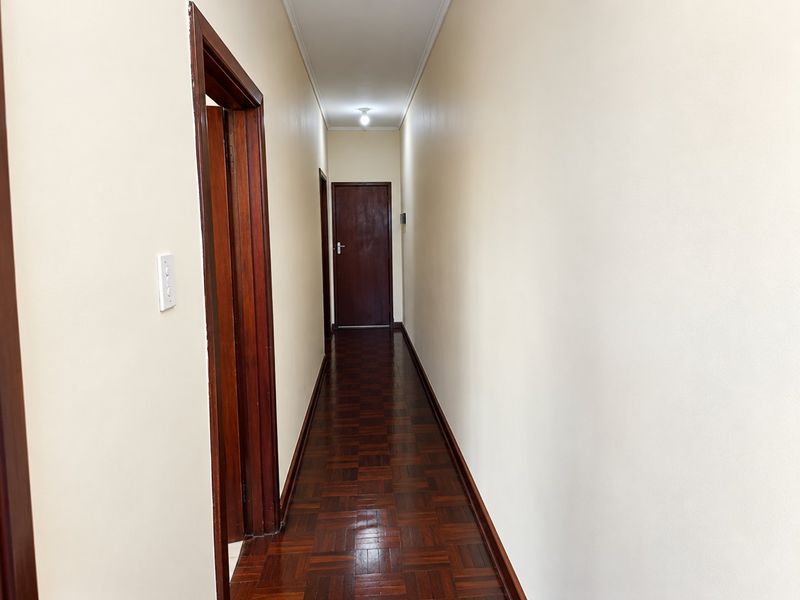 A clean, empty hallway featuring polished parquet flooring and traditional timber door frames, providing access to various rooms within the apartment.