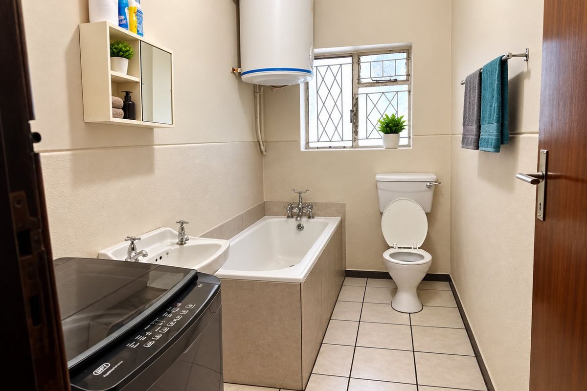 A functional bathroom featuring a bathtub, pedestal basin, toilet, and an electric water heater, with tiled flooring and security bars on the window.