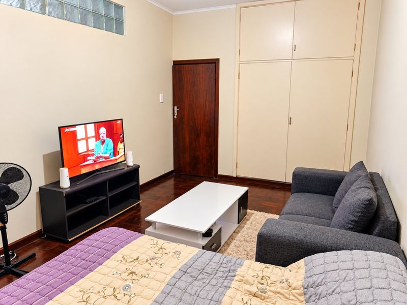 A bedroom featuring parquet flooring, built-in cupboards, and a high-level glass block window, providing a functional and well-maintained living space.