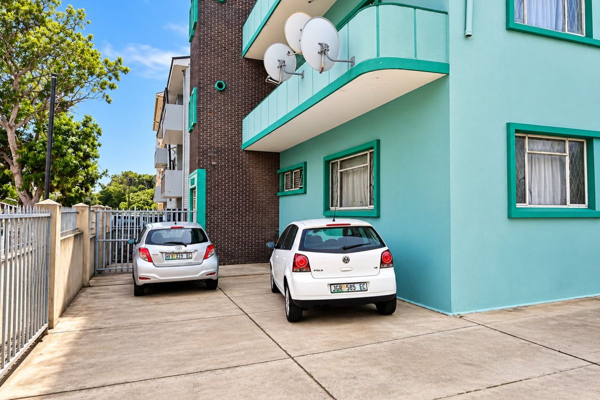 Rear exterior view of the apartment building featuring a concrete driveway, secure gated access, and balconies with satellite dish installations.