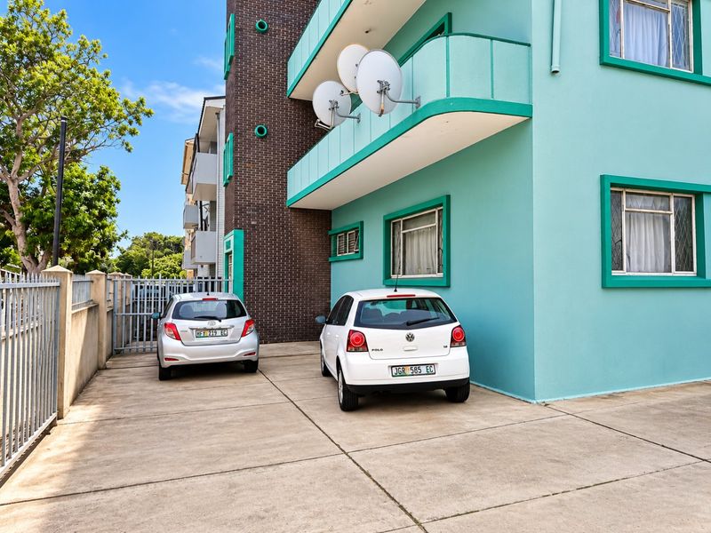 Rear exterior view of the apartment building featuring a concrete driveway, secure gated access, and balconies with satellite dish installations.