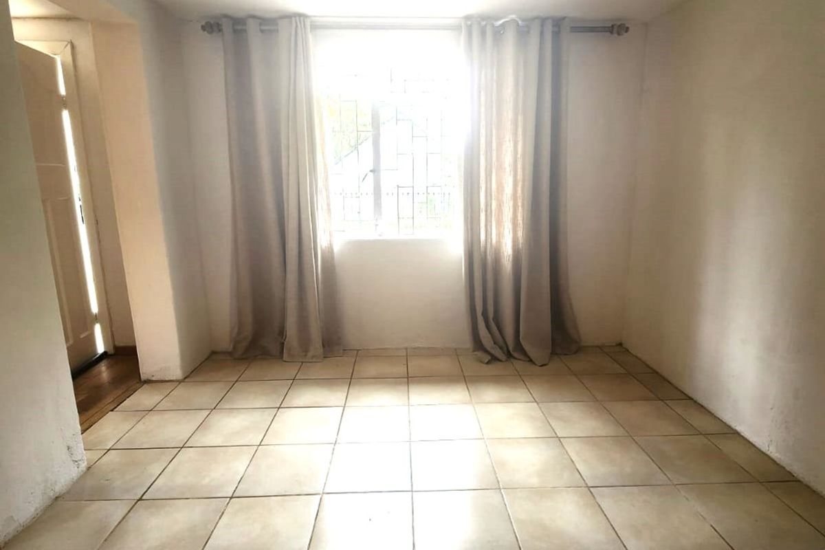 An empty living room featuring tiled flooring and a window with security bars, offering a blank canvas for interior design.