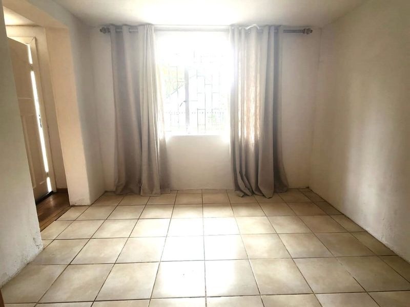 An empty living room featuring tiled flooring and a window with security bars, offering a blank canvas for interior design.