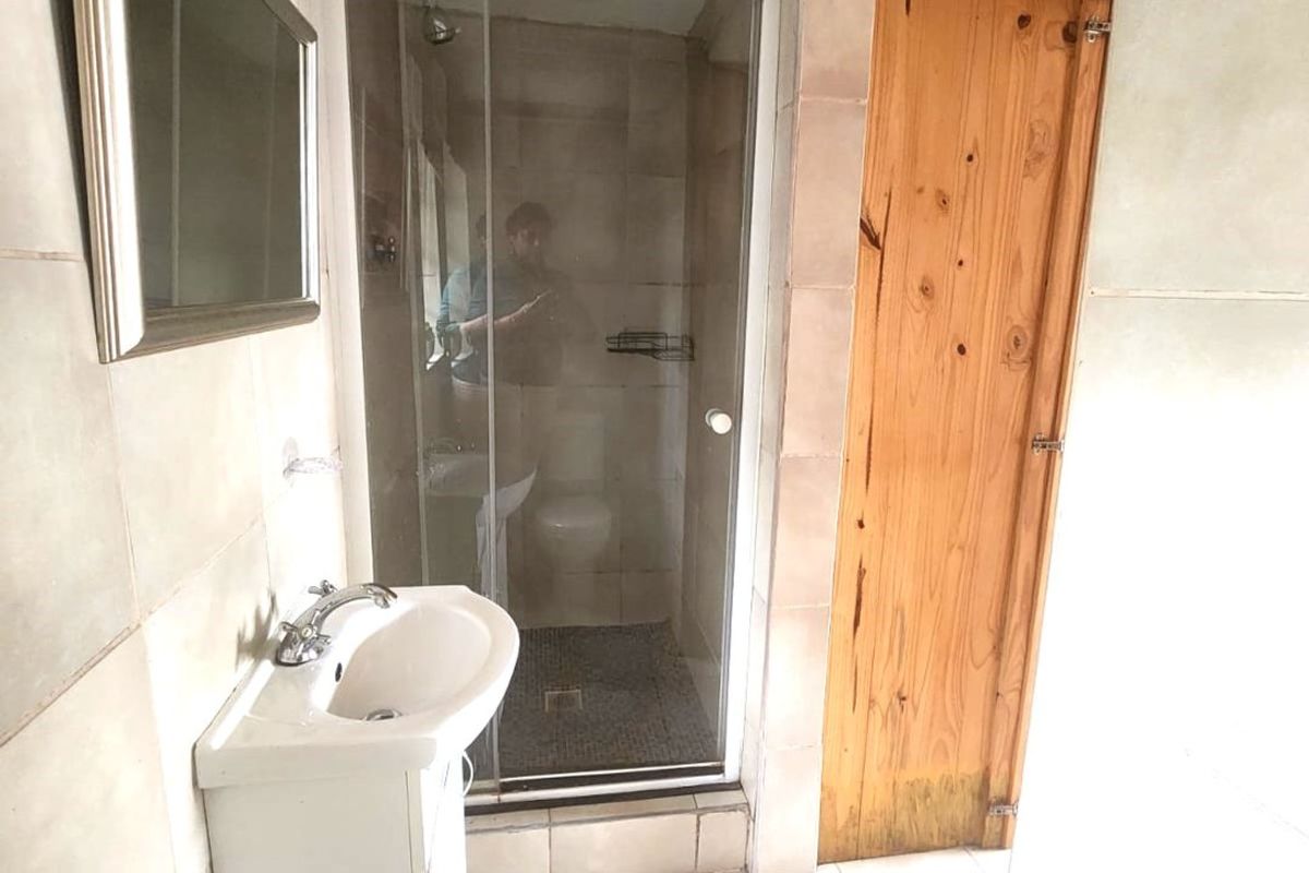 A functional bathroom featuring a shower enclosure, pedestal basin, and neutral wall and floor tiling.
