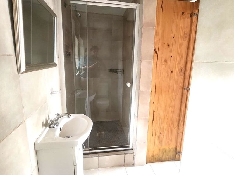 A functional bathroom featuring a shower enclosure, pedestal basin, and neutral wall and floor tiling.
