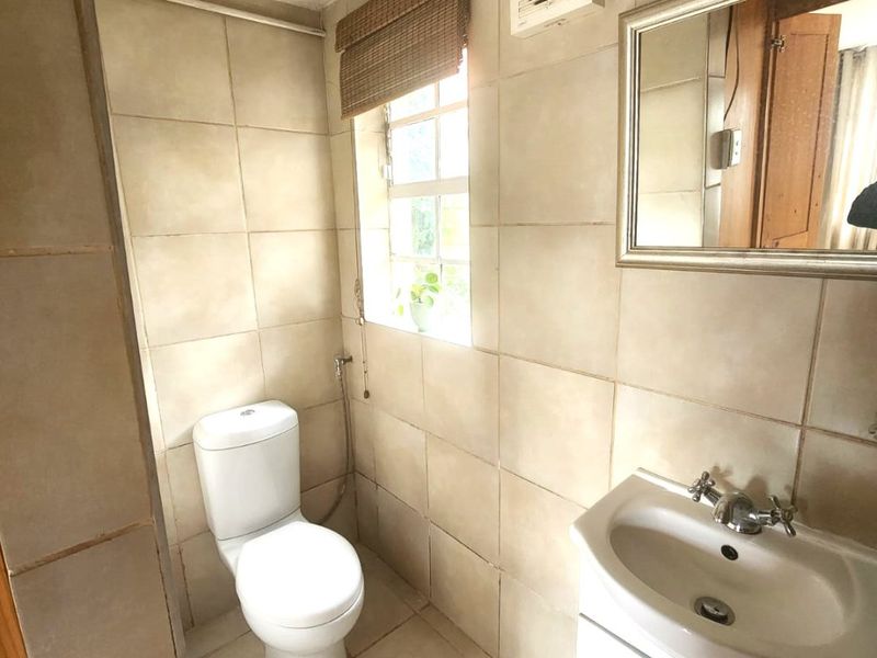 A compact bathroom featuring tiled walls and flooring, a white toilet, and a vanity basin with an integrated extractor fan.
