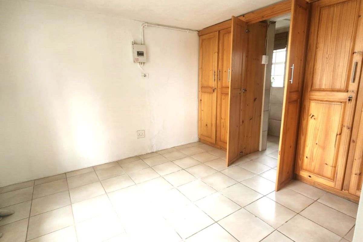 An empty bedroom featuring tiled flooring and built-in wooden cupboards, with an exposed electrical distribution board on the wall.