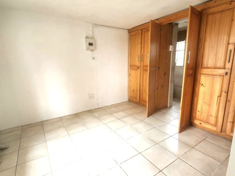 An empty bedroom featuring tiled flooring and built-in wooden cupboards, with an exposed electrical distribution board on the wall.