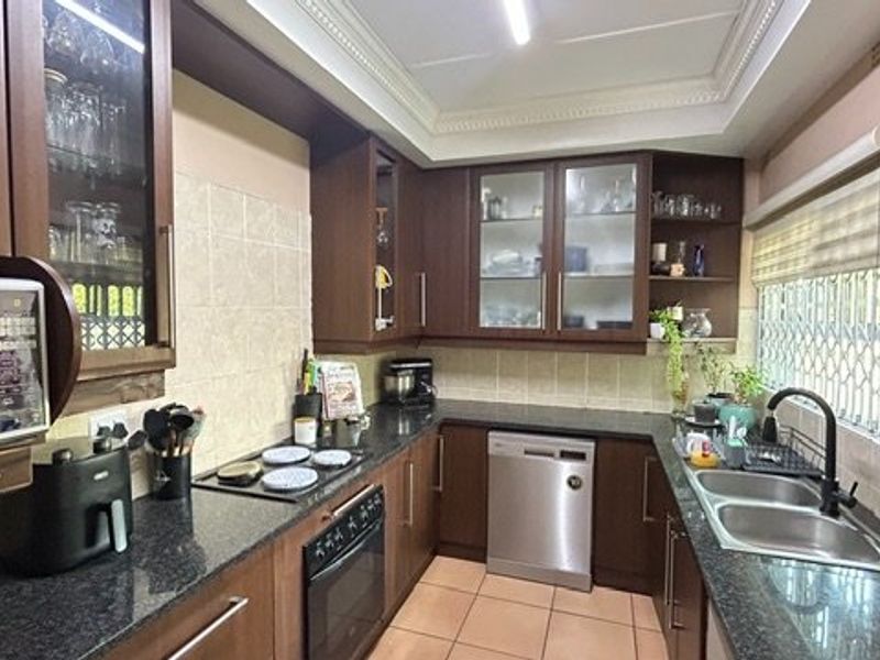 A functional kitchen featuring dark wood cabinetry, granite countertops, built-in oven, hob, and a double sink with a modern mixer tap.