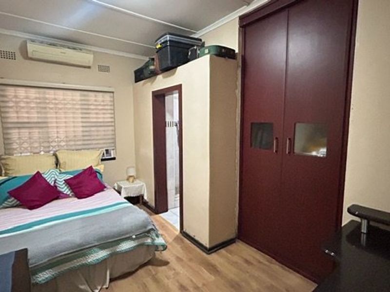 A functional bedroom featuring laminate flooring, a built-in wardrobe, and a wall-mounted split-system air conditioner.