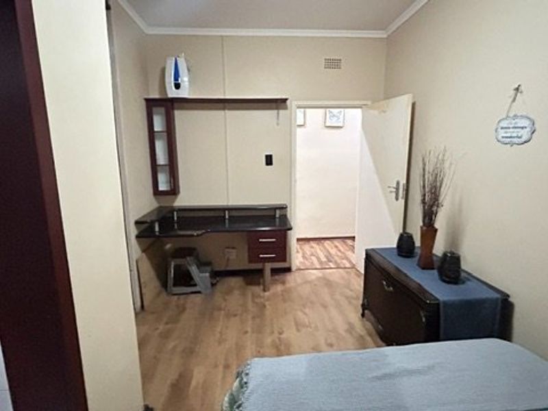 A bedroom featuring laminate flooring and a built-in desk area, providing a functional space with direct access to an adjoining room.