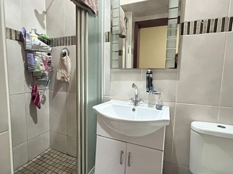 A compact bathroom featuring a shower enclosure, vanity basin, and toilet with neutral wall tiling.