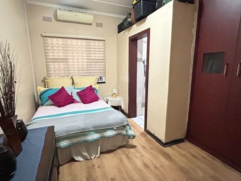 A compact bedroom featuring laminate flooring, a built-in wardrobe, and a wall-mounted air conditioning unit.
