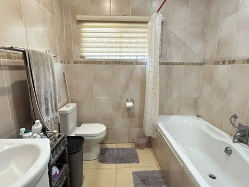 A functional bathroom featuring a bathtub with shower mixer, pedestal basin, and neutral wall and floor tiling.