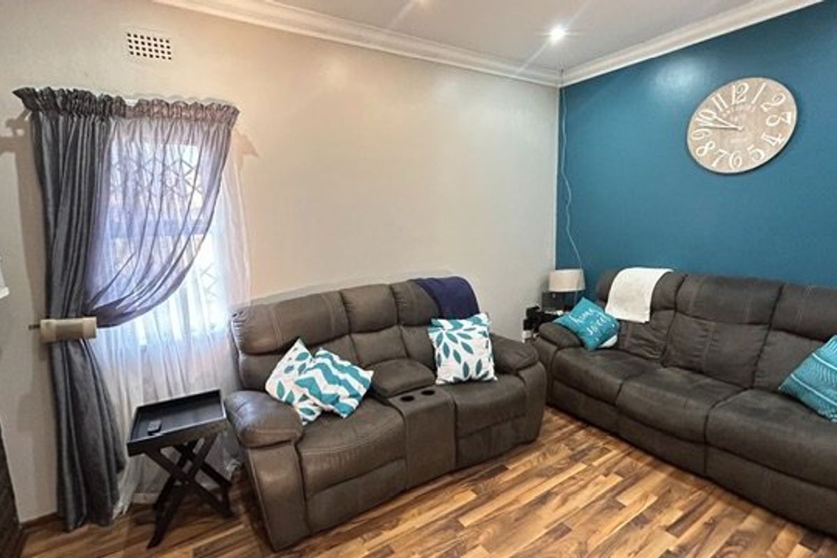 A comfortable living room featuring laminate flooring, decorative cornicing, and a bold blue accent wall, providing a functional and inviting space.