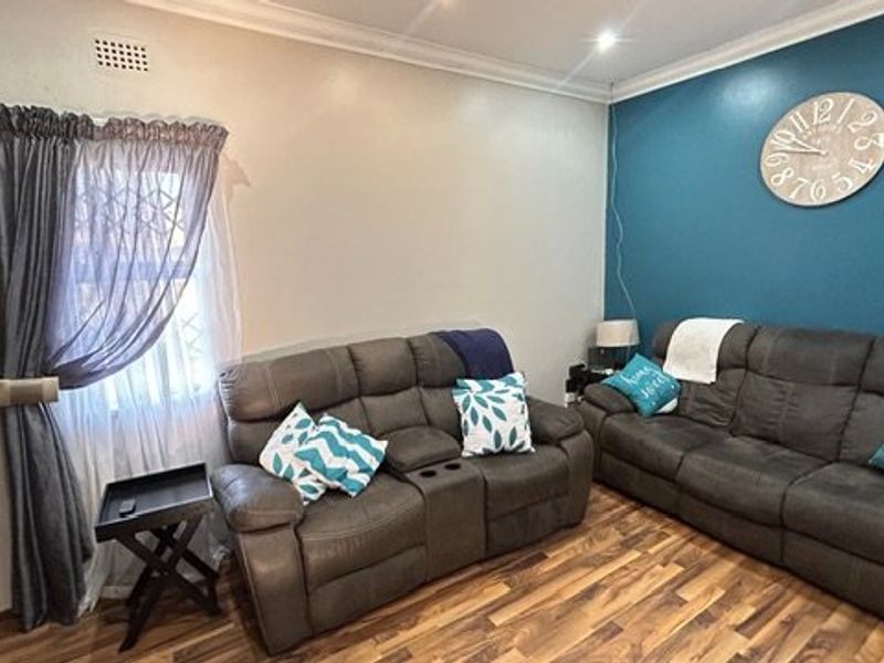 A comfortable living room featuring laminate flooring, decorative cornicing, and a bold blue accent wall, providing a functional and inviting space.