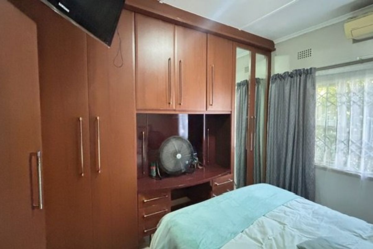 A bedroom featuring extensive built-in wooden cabinetry with an integrated vanity unit, split-system air conditioning, and security bars on the window.