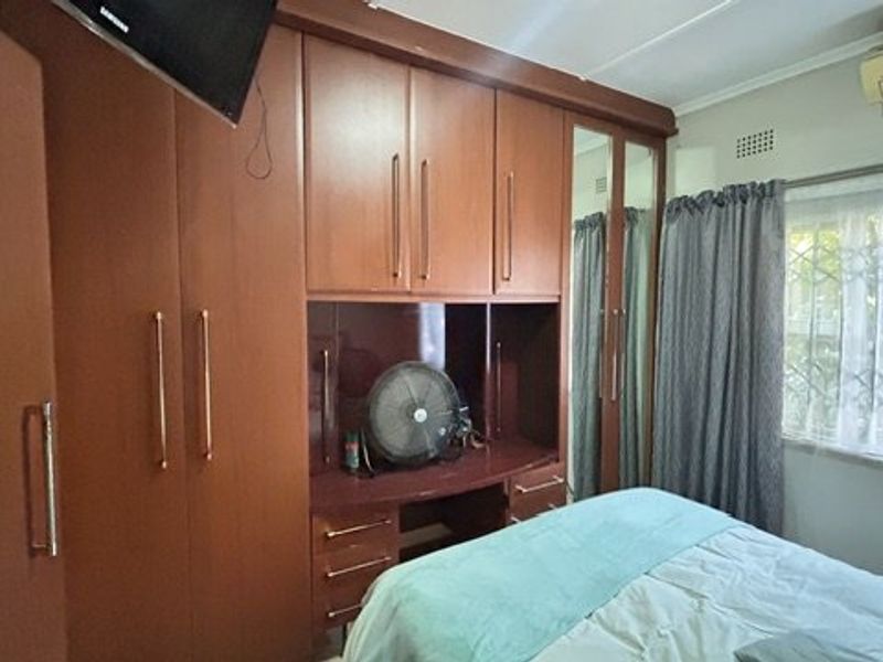 A bedroom featuring extensive built-in wooden cabinetry with an integrated vanity unit, split-system air conditioning, and security bars on the window.