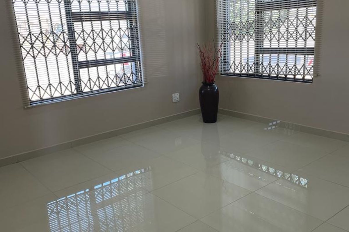 A bright, empty living room featuring polished porcelain floor tiles, security bars on windows, and modern recessed downlighting.