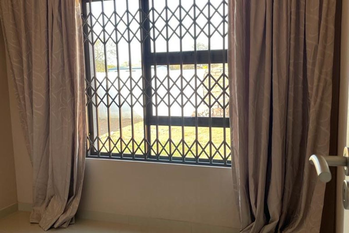 A bright, empty bedroom featuring polished tiled flooring, neutral walls, and a window fitted with a security gate and curtain tracks.