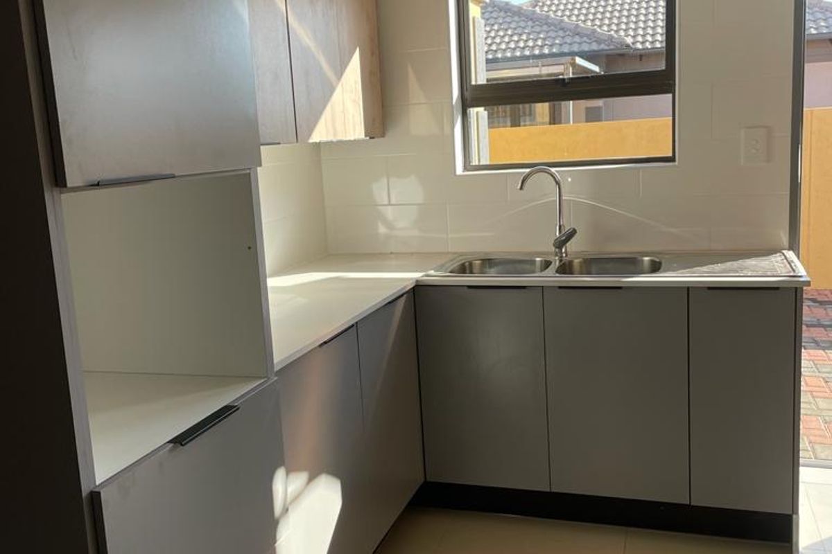 A modern, empty kitchen featuring sleek grey and wood-tone cabinetry, a double sink, and tiled flooring with natural light.