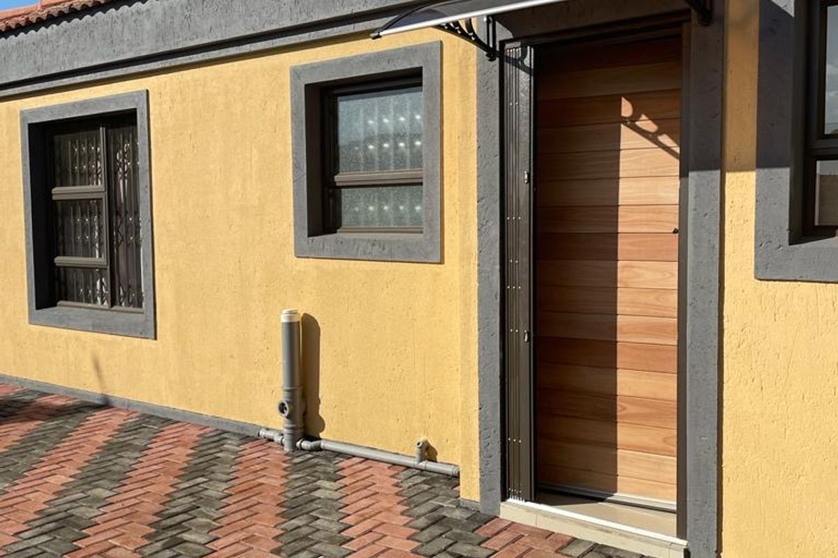 Exterior view of the property featuring a textured yellow facade, terracotta roof tiles, a modern timber door with an awning, and paved ground.