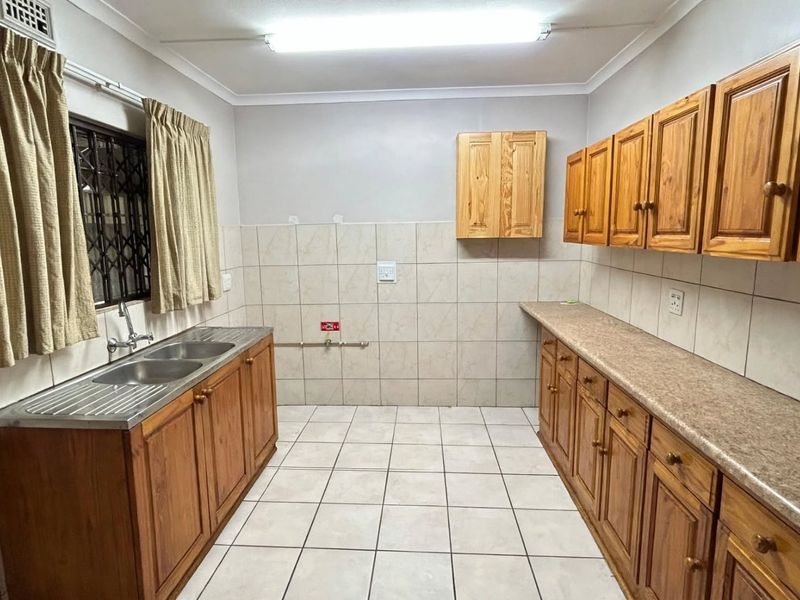 A functional scullery or laundry area featuring wooden cabinetry, laminate countertops, a double stainless steel sink, and tiled finishes throughout.