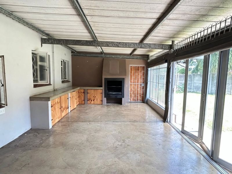 Covered patio area featuring a built-in braai, concrete countertops with wooden cabinetry, and large sliding glass doors opening to the garden.