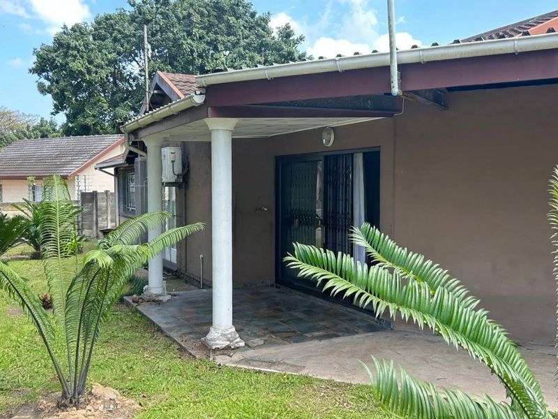 A covered patio area featuring tiled flooring and concrete columns, providing direct access to the garden through a sliding glass door.