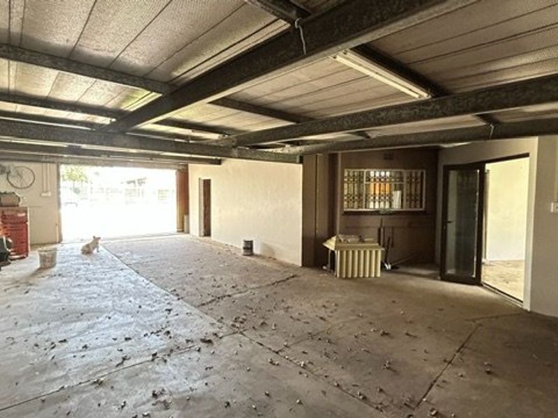 A spacious, open-plan garage featuring exposed steel beam ceiling construction and concrete flooring, offering significant potential for storage or workshop conversion.