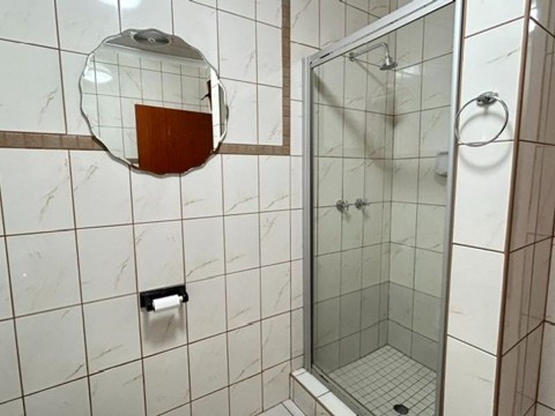 A functional bathroom featuring a glass-enclosed shower, tiled walls, and standard sanitary fixtures.